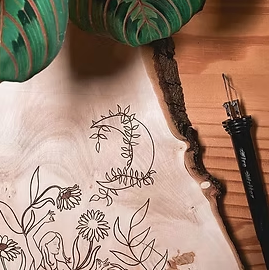 An image depicting a piece of half finished pyrography art. There is a pyrography tool on the table next to the piece.